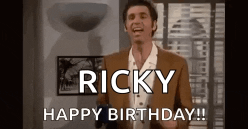 a man in a suit and white shirt is standing in front of a window and says `` ricky happy birthday ! ''