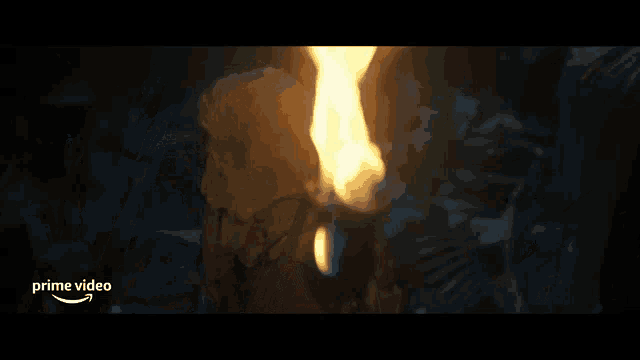 a man in a hood is holding a torch in front of a fire and the words prime video are on the bottom