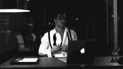 a black and white photo of a man sitting at a desk with an apple laptop