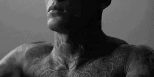 a man with a lot of tattoos on his chest and neck is smoking a cigarette .
