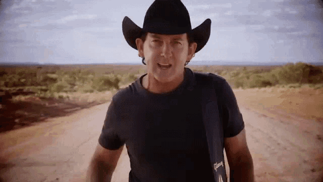 a man wearing a cowboy hat is standing on a dirt road .