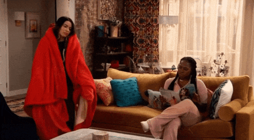two women wrapped in red blankets are standing next to each other in a living room