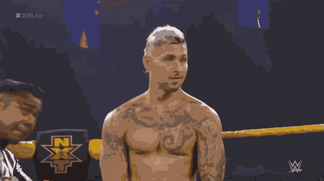 a shirtless wrestler stands in a wrestling ring with a nxt logo