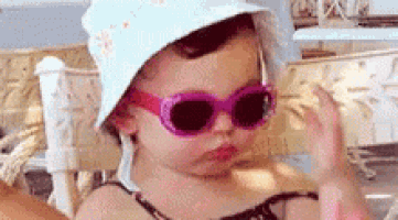 a little girl wearing sunglasses and a hat is giving the middle finger .