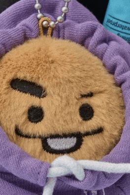 a stuffed animal is wearing a purple hoodie with a smiley face on it .