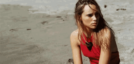 a woman in a red top is sitting on the beach looking at the camera .