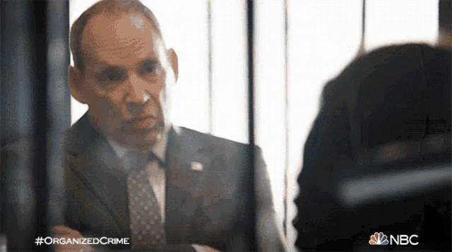 a man in a suit and tie is talking to another man in a jail cell with #organizedcrime written on the bottom