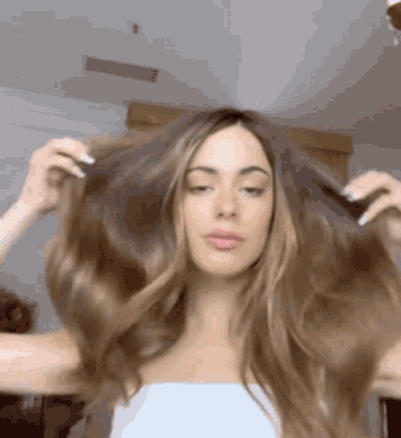 a woman with long brown hair is holding her hair in a room .