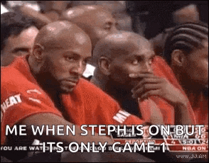 a group of men are sitting in a stadium watching a basketball game and one of them is covering his mouth with his hand .