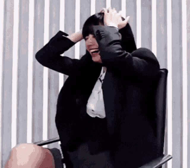 a woman in a business suit is sitting in a chair with her hands on her head .