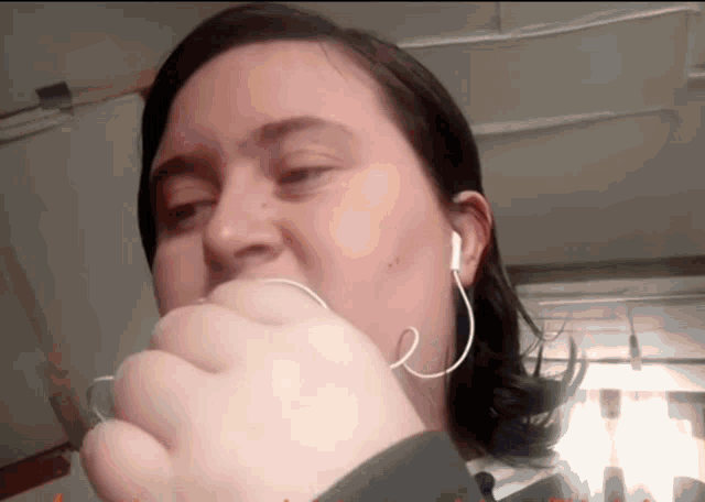 a woman wearing ear buds is covering her mouth with her hand