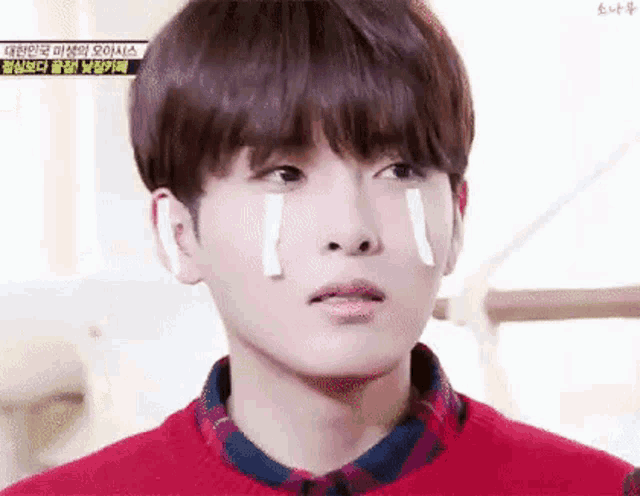 a young man with tears coming out of his eyes is wearing a red sweater and a plaid shirt .