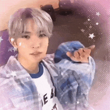 a young man wearing a plaid jacket and a white shirt is making a heart shape with his hand .