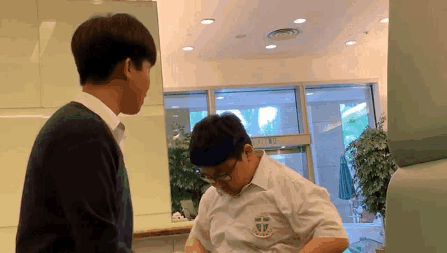 a man wearing a white shirt with a cross on it is talking to another man