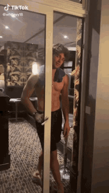 a man without a shirt is standing in a doorway holding a glass of wine .