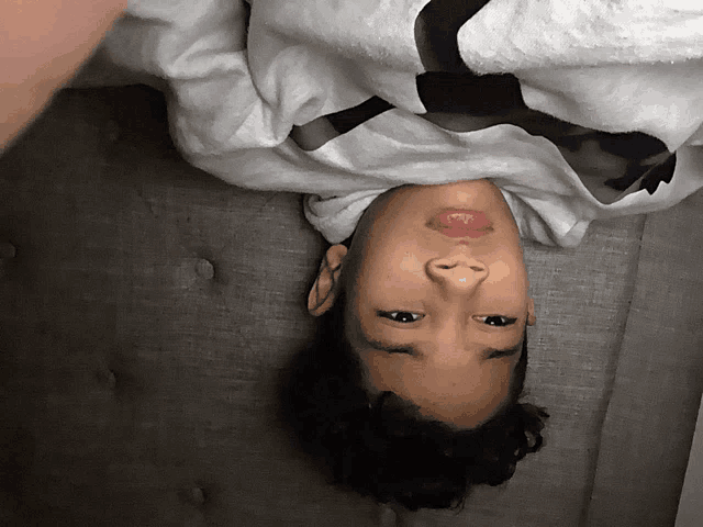 a young boy is laying upside down on a couch with his head down