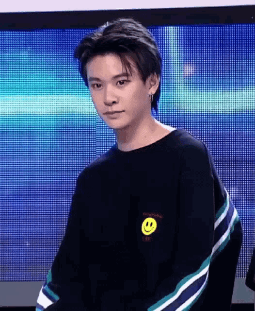 a young man wearing a black sweater with a yellow smiley face on the front .