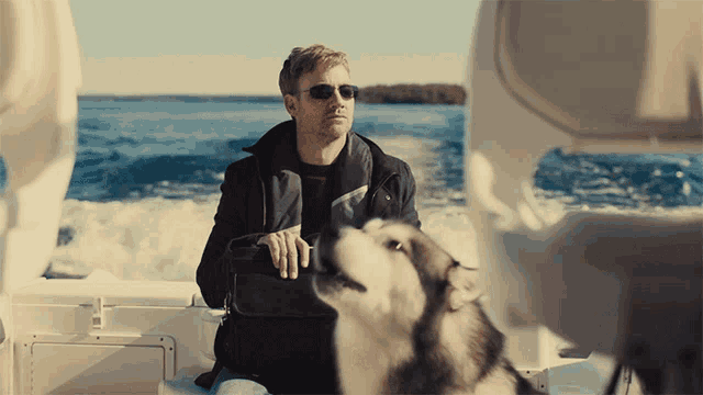 a man in sunglasses sits on a boat with a dog licking his face