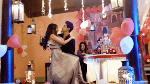 a man holds a woman in his arms in a room decorated with balloons and lights