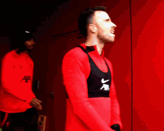 a man wearing a red shirt with a black nike vest on his back