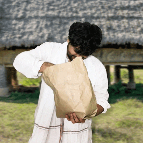 a man in a white robe holds a brown paper bag