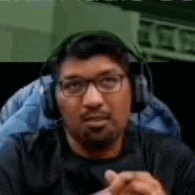a man wearing headphones and glasses is sitting in a chair with his hands folded .