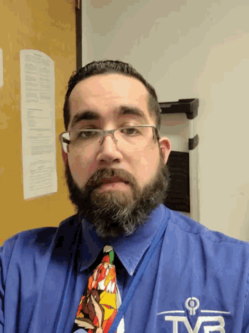 a man with a beard wearing glasses and a blue shirt that says tf