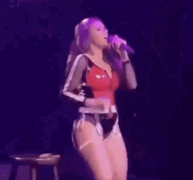a woman in a red top and white shorts is singing into a microphone on stage .