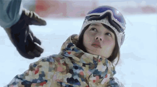 a young girl wearing a helmet and goggles is laying in the snow