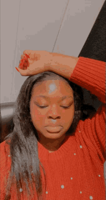 a woman wearing a red sweater with pearls on it holds her hand to her forehead