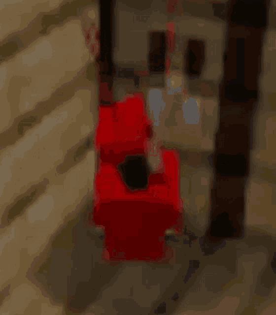 a red block is sitting on a wooden floor next to a brick wall .