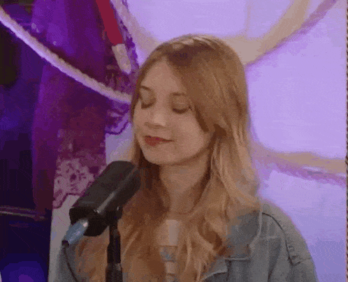 a woman is singing into a microphone with her eyes closed and smiling .