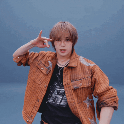 a man wearing a brown jacket and a black shirt with the letter h on it is dancing
