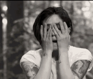 a woman with tattoos is covering her face with her hands .
