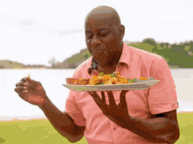 a man in a pink shirt holds a plate of food in his hands