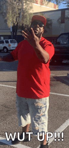 a man in a red shirt and hat is standing in a parking lot with the words wut up written below him