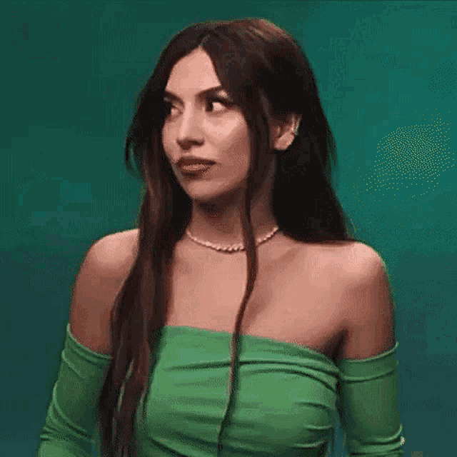 a woman wearing a green off the shoulder top and a pearl necklace .