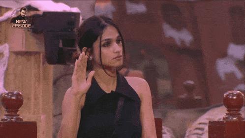 a woman in a black dress is sitting in front of a screen that says new episode on it