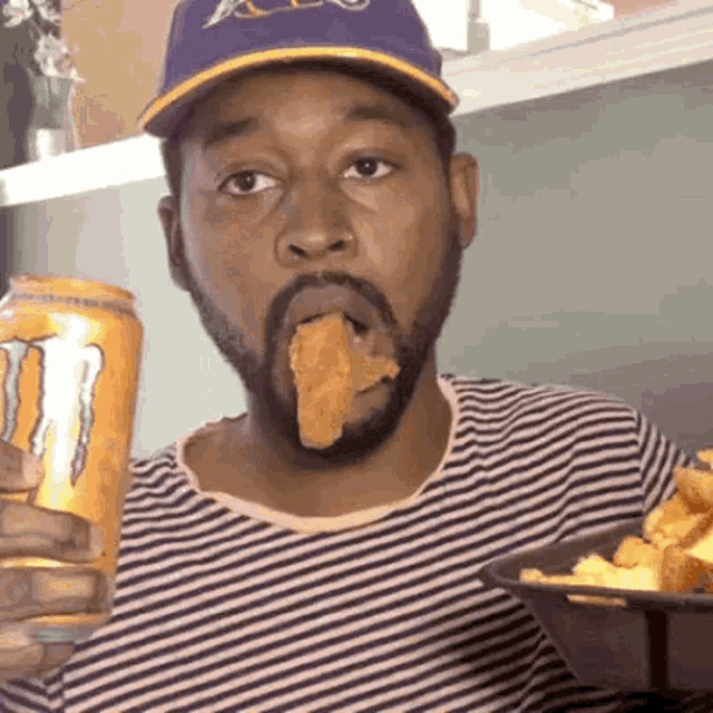 a man with a beard is eating chicken and drinking a can of monster energy drink .