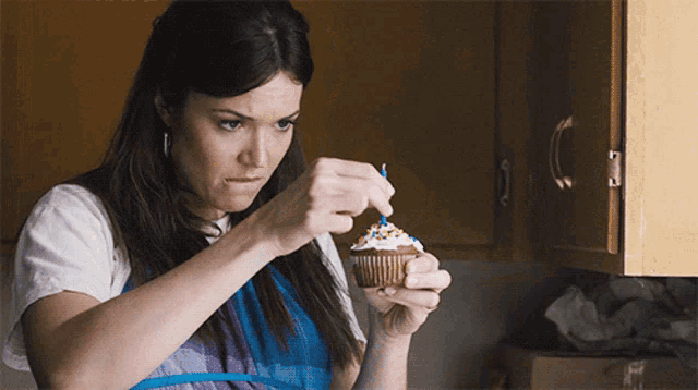 a woman is decorating a cupcake with a blue candle