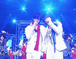 two men singing into microphones on a stage in front of a blue background