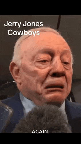 jerry jones is crying while talking into a microphone while wearing a suit and tie .