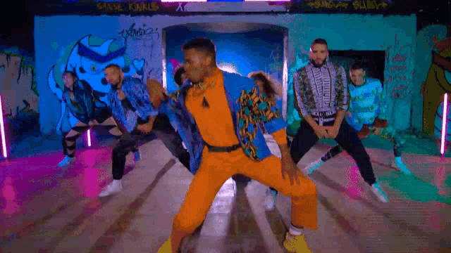 a group of people are dancing in front of a wall that has graffiti on it including the word kinks