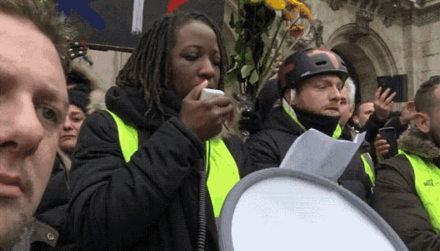 a woman in a yellow vest is talking on a cell phone while a man holds a megaphone