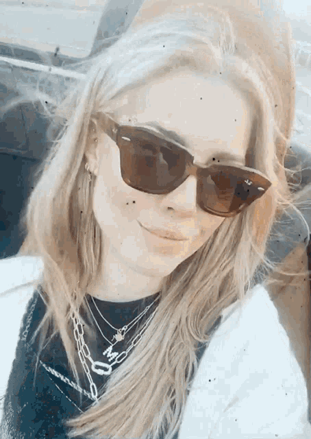 a woman wearing sunglasses and a necklace with a letter m on it