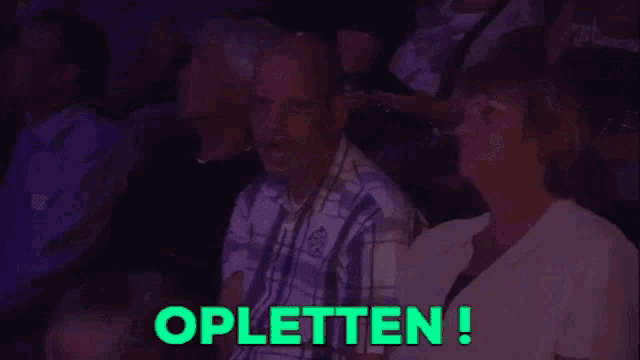 a man and woman are sitting in a dark room with the word opletten written in green