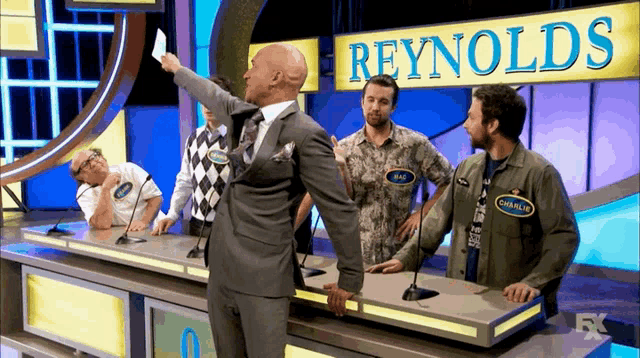 a group of men are playing a game show with a sign that says reynolds