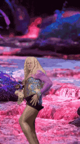 a woman in a purple top and shorts is dancing in front of a pink waterfall .