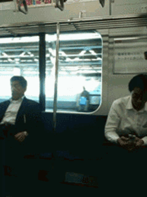 a man in a suit sits next to another man in a white shirt on a subway