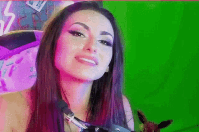 a woman is sitting in front of a green screen holding a stuffed animal and smiling .